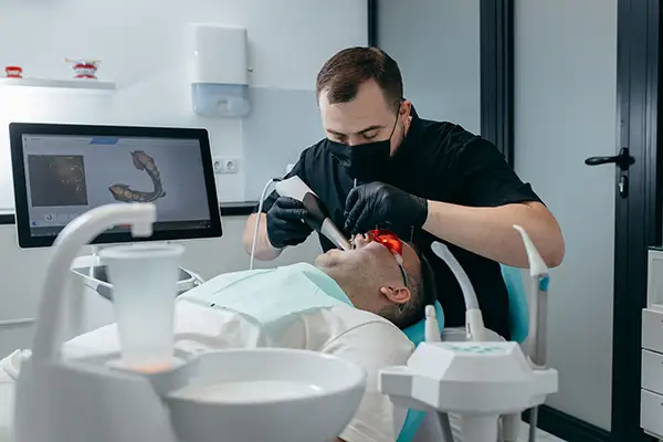 Dentist performing a digital impression scan on a patient using advanced scanning technology, with a monitor displaying 3D images of the patient's teeth.